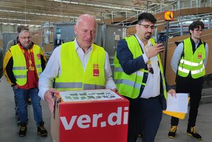 Berlins Bürgermeister Kai Wegner hält wenig glücklich ein Paket in der Hand, auf dem der Name der Gewerkschaft Verdi steht