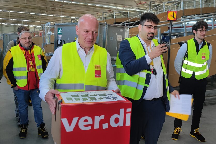 Berlins Bürgermeister Kai Wegner hält wenig glücklich ein Paket in der Hand, auf dem der Name der Gewerkschaft Verdi steht