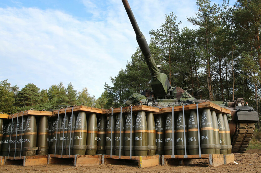 Paletten voller Munition stehen vor einer Panzerhaubitze