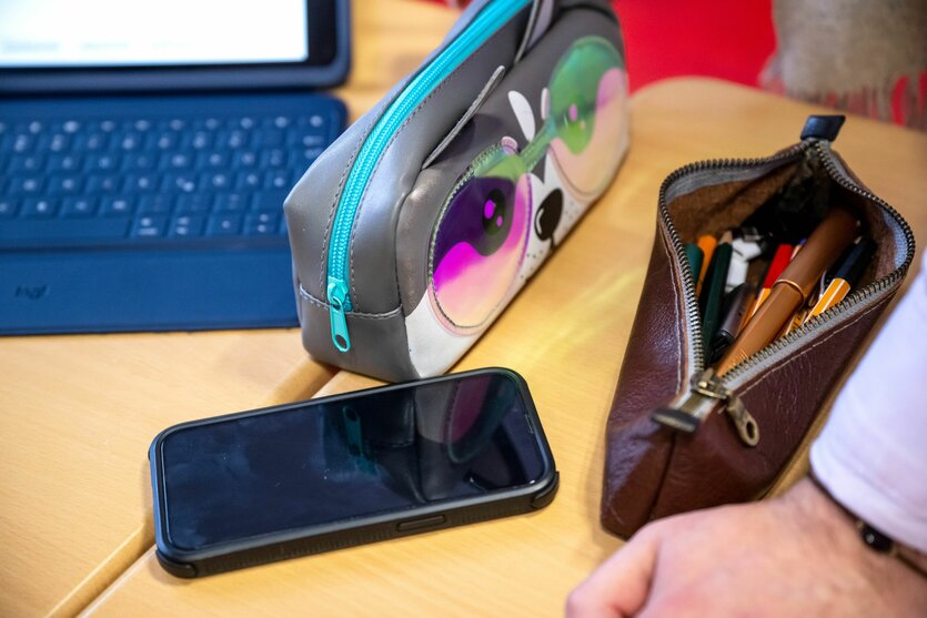 Ein Smartphone liegt neben einem Federmäppchen auf einer Schulbank