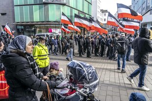 Die Neonazi Gruppe Jung und Stark, JS, demonstriert in der Innenstadt von Essen, fordern Remigration; eine Frau mit Kinderwagen und Kopftuch beobachtet die Nazis