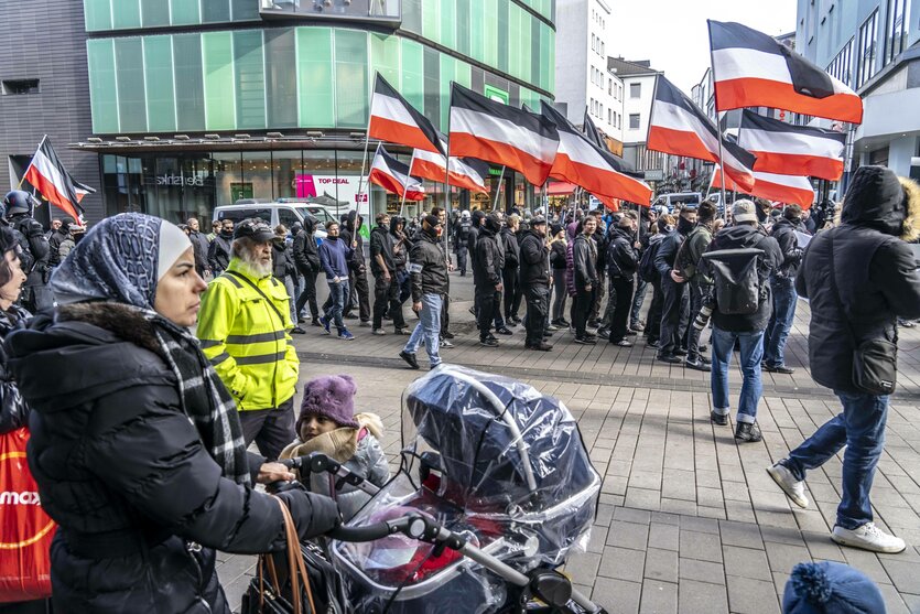 Die Neonazi Gruppe Jung und Stark, JS, demonstriert in der Innenstadt von Essen, fordern Remigration; eine Frau mit Kinderwagen und Kopftuch beobachtet die Nazis