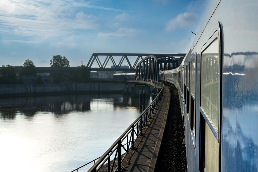 Fahrt über eine Eisenbahnbrücke, der etwas ältere Nightjet in blau is rechts im Bild, unter der Brücke ist Wasser, darüber der Himmel