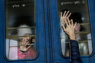 Ein Mann drückt seine Hand auf die Fensterscheibe eines Zuges, um sich von zwei Kindern zu verabschieden