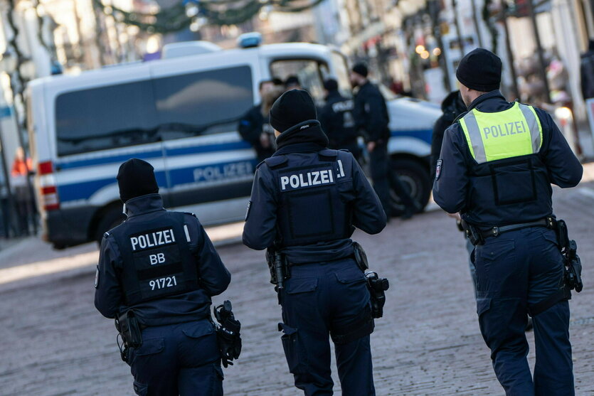 Drei Personen in Polizeiuniform von hinten gesehen, vor ihnen ein Gruppenfahrzeug