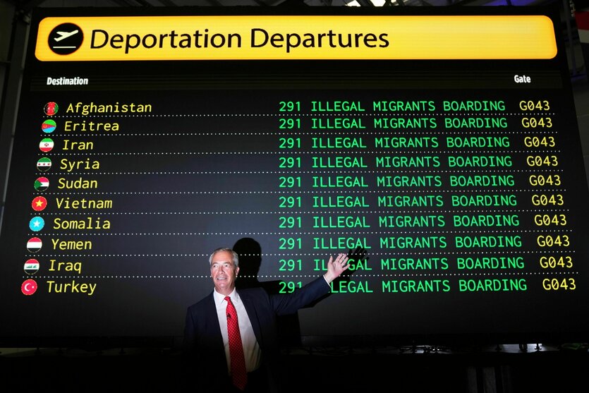 Nigel Farage vor einer "Abflugtafel" stolz und freudig blickend