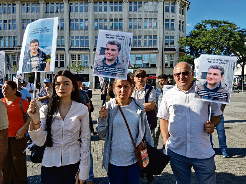 Drei Menschen stehen mit Schildern auf der Straße bei einer Demonstration gegen die Abschiebung von Mehmet Çakas