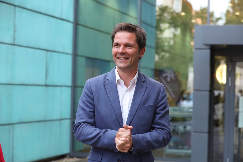 Steffen Krach steht vor einem Gebäude und lacht