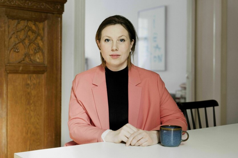 Eine Frau in lachsfarbenem Blazer sitzt am Tisch