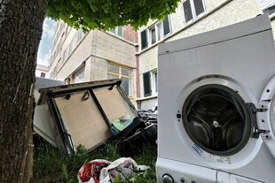 Ein Haufen Müll, bestehend aus Sperrgut wie einer kaputten Waschmaschine, steht vor einem innerstädtischen Mietshaus.