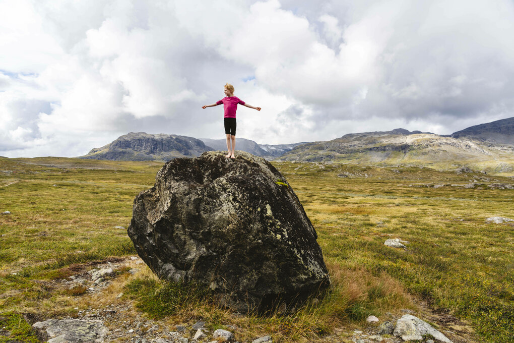 Tundra, ein großer Felsen, eine person in lila Tshirt steht die Arme ausgebreitet darauf