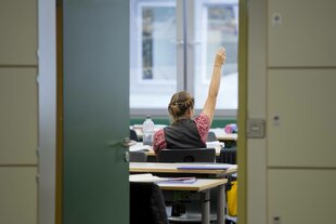 Eine Schuelerin meldet sich waehrend einer Unterrichtsstunde , Blick durch eine offene Tür und von Hinten