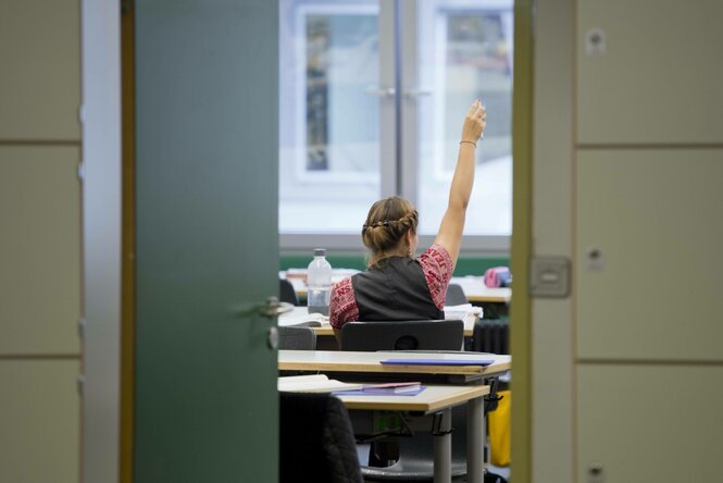 Eine Schuelerin meldet sich waehrend einer Unterrichtsstunde , Blick durch eine offene Tür und von Hinten