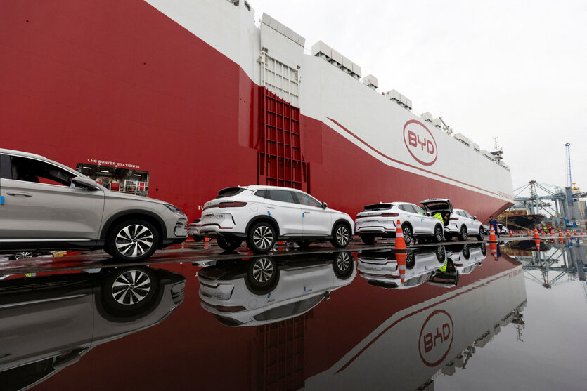 E-SUVs der Marke BYD stehen für die Verladung auf einem YD Autofrachter bereit und spiegeln sich in einer Pfütze