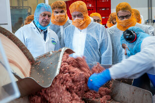 Alois Rainer steht mit Hygeneschutz vor einem offenen Cutter mit ordentlich Fleisch beim Betriebsrundgang im Unternehmen Ludwigsluster Fleisch- und Wurstwaren