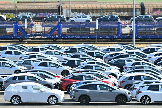 Neue Elektroautos der verschiedenen VW-Konzernmarken parken auf einem Platz am Volkswagen-Werk, im Hintergrund fährt ein Zug mit Autos beladen