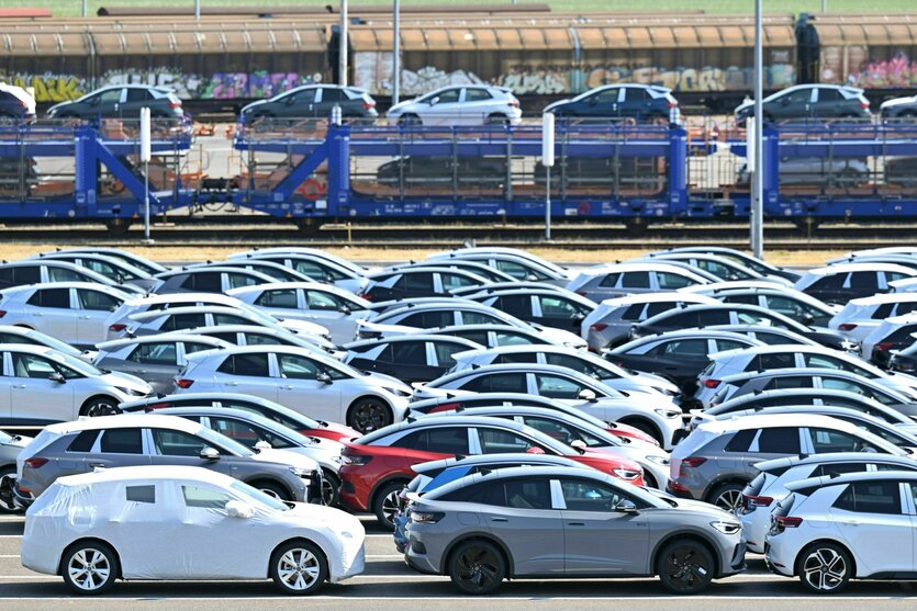 Neue Elektroautos der verschiedenen VW-Konzernmarken parken auf einem Platz am Volkswagen-Werk, im Hintergrund fährt ein Zug mit Autos beladen