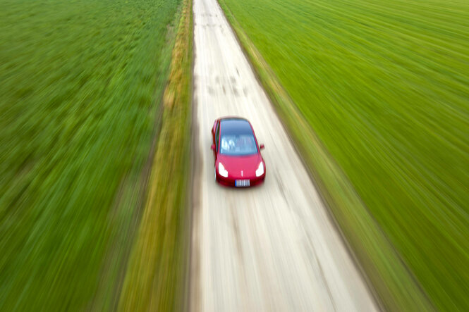 Roter Sportwagen zieht mit hoher Geschwindigkeit durchs Grüne auf einer Landstraße aus der Vogelperspektive
