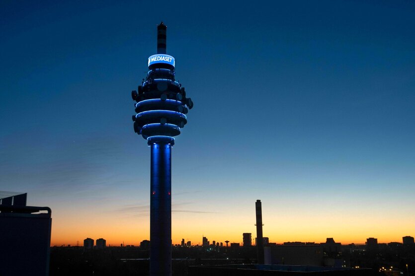 Ein hoher Turm mit der Leuchtschrift Mediaset an der Kuppel steht in der Abenddämerung und überragt die Stadt