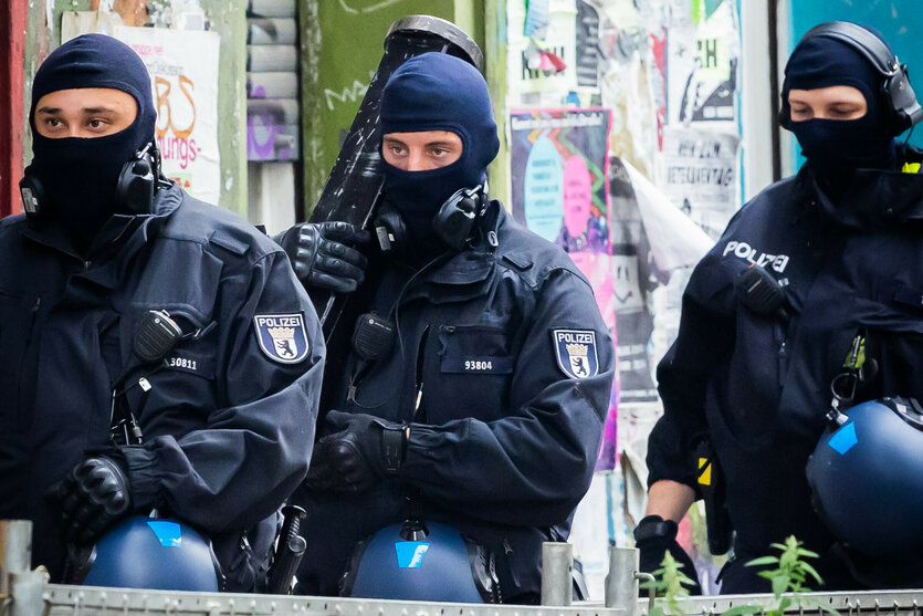Drei Polizisten mit vermummten Gesichtern und einer Ramme