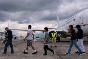 Mehrere Männer laufen über ein Rollfeld, im Hintergrund ein parkendes Flugzeug