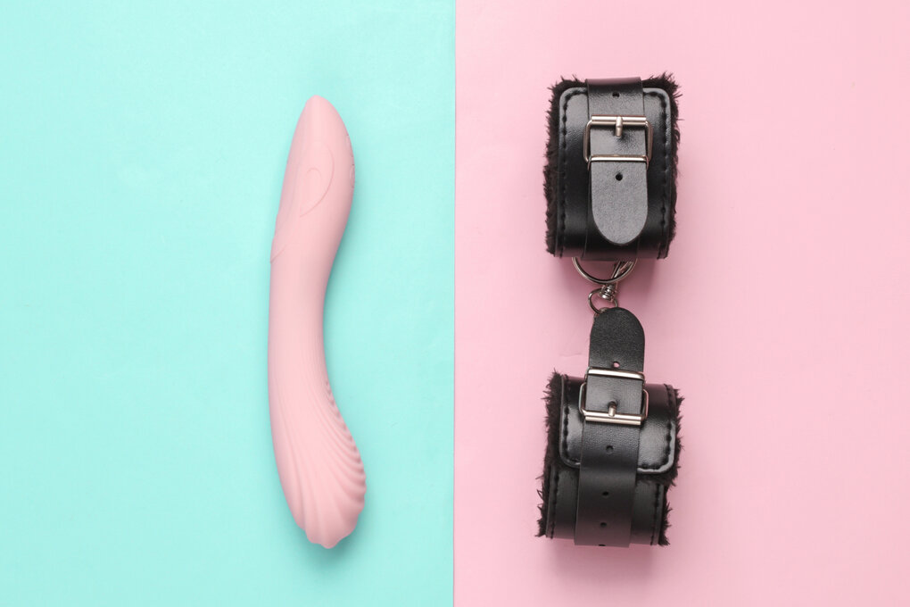 Lederhandschellen mit Dildo-Vibrator auf blau-rosa Pastellhintergrund