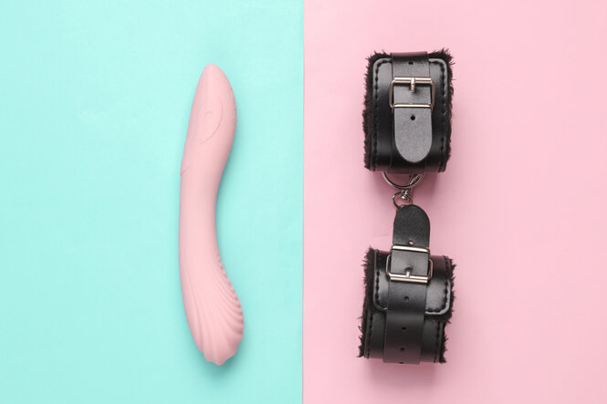 Lederhandschellen mit Dildo-Vibrator auf blau-rosa Pastellhintergrund