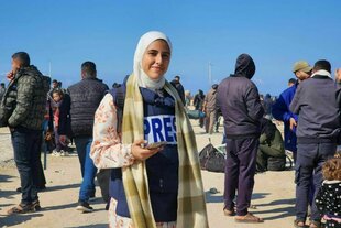 Porträt von Malak Tantesh - sie steht auf einem belebten Platz und trägt eine Weste mit der Aufschrift Press
