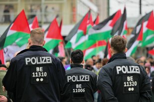 Polizisten beobachten einen Demonstrationszug mit Palästina-Flaggen