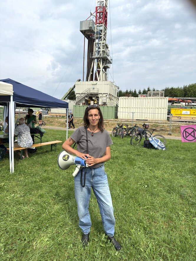 Claudia Danner steht in Jeans und T-Shirt vor dem Bohrturm und trägt ein Megaphon