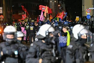 Demonstrationszug in nächtlicher Straße mit vielen Flaggen, von Polizei umstellt