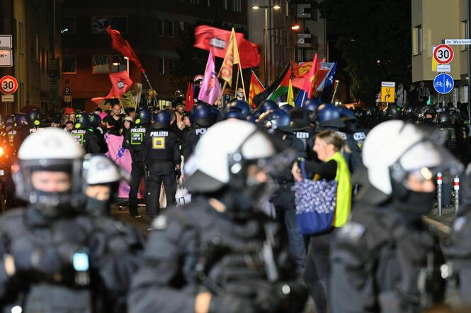 Demonstrationszug in nächtlicher Straße mit vielen Flaggen, von Polizei umstellt