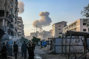 Rauchsäule steigt hinter zerbombter Stadt auf