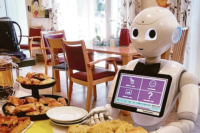Der Pflegeroboter Charlie steht an einem Tisch mit Kuchen und Gebäck.
