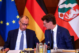 Merz und Wüst sitzen nebeneinander, einer von ihnen verzieht den Mund zu einer 'Schnute' (es ist Merz)