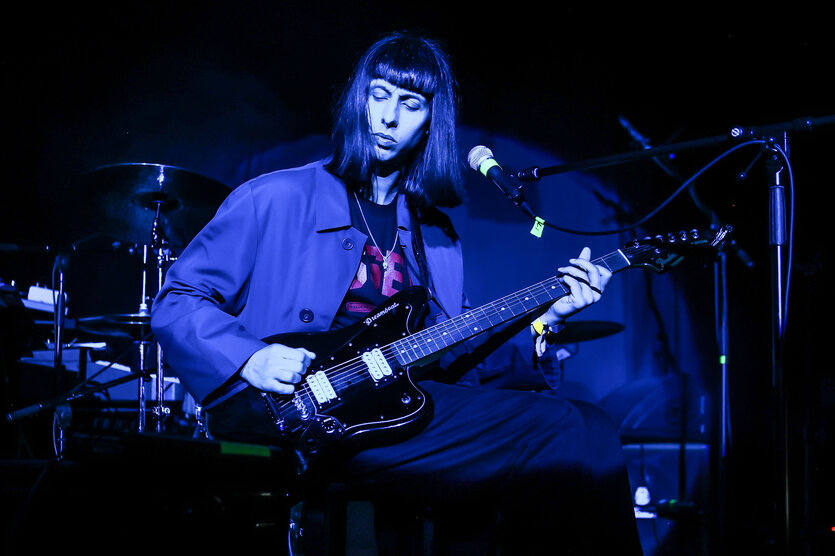 Eine dunkelhaarige Frau an der E-Gitarre in blauem Licht