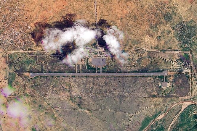 Eine Luftaufnahme zeigt einen Flughafen nach einem Militärangriff. Es steigt Rauch auf