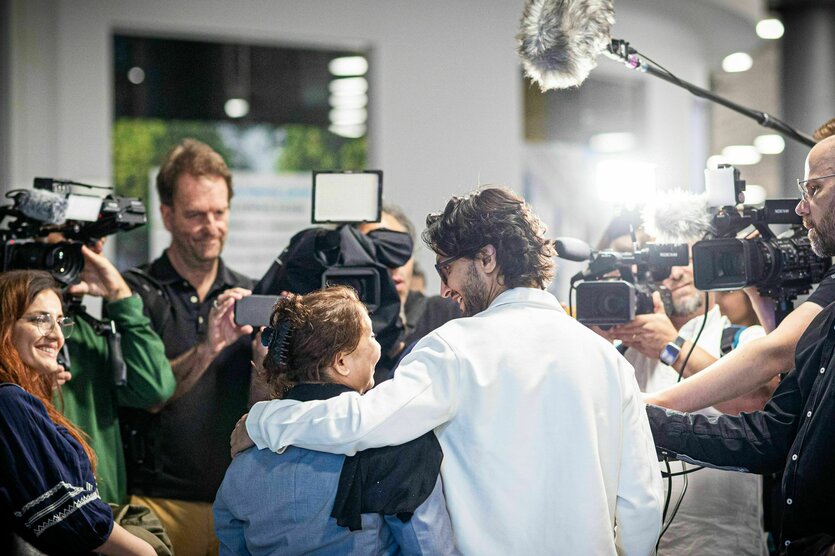 Zwei Personen stehen Arm in Arm vor einer Gruppe von Journalisten