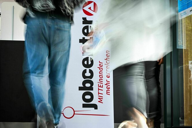 Zwei Personen laufen auf ein Schild zu, auf dem steht: "Jobcenter"