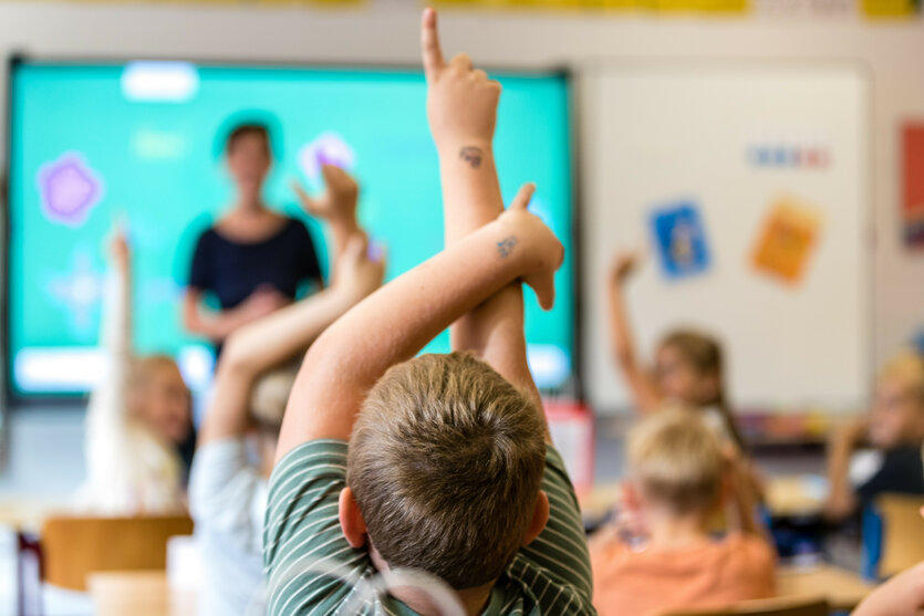 Klassenraumszene, Lehrerin vor Schüler:innen, mehrere melden sich