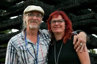 Horst und Birgit Lohmeyer stehen vor einem Mahnmal, bestehend aus verkohlten Balken ihrer abgebrannten Scheune