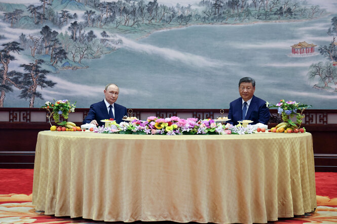 Putin und Xi sitzen an einem Tisch der mit Blumen und Obst gedeckt ist - der Tisch ist rund und groß