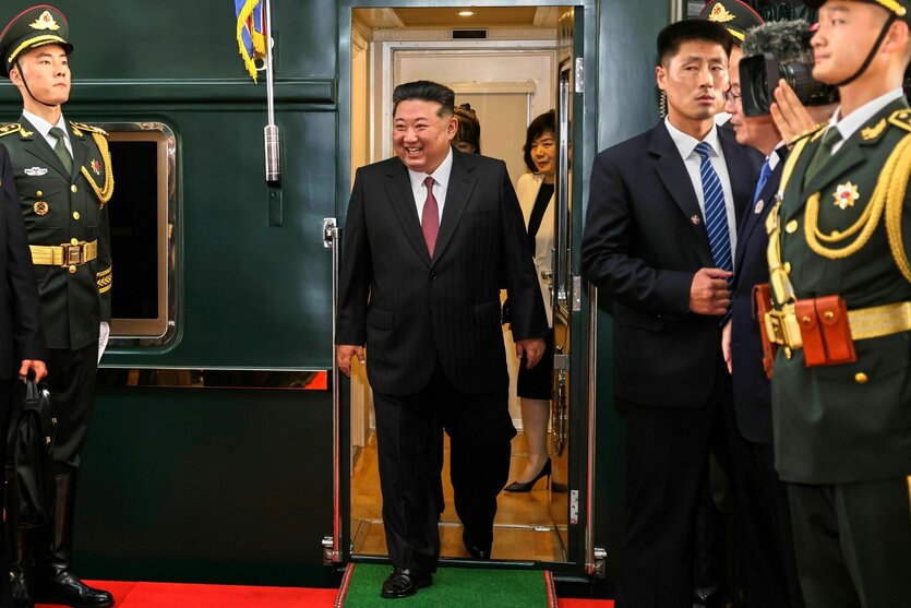 Kim Jong Un geht durch eine Tür im Zug, die von Militärs bewacht wird. Er scheint bester Laune zu sein und lacht