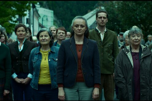 Filmstill: Eine Menschenmenge in einem Dorf schaut richtung Kamera