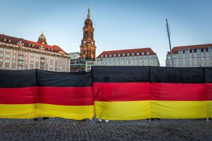 Ein riesiges Banner in Deutschlandfarben verdeckt halb eine Stadtsilhouette