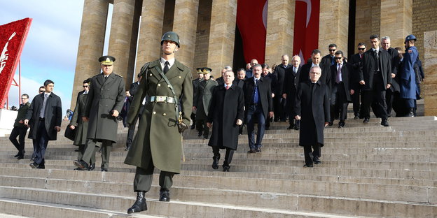 Soldaten und Politiker schreiten die Treppen eines Mausoleums hinunter