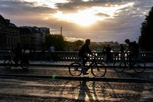 Menschen fahren bei Sonnenuntergang mit dem Fahrrad auf einer Brücke über die Seine