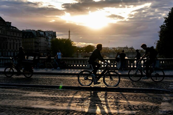 Menschen fahren bei Sonnenuntergang mit dem Fahrrad auf einer Brücke über die Seine