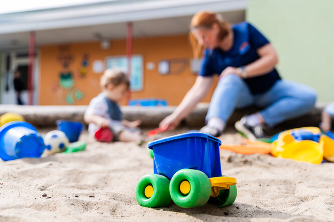 Kind und erwachsener Mensch buddeln in einem Sandkasten