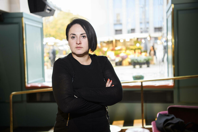 Eine Frau steht mit verschrenkten Armen vor einem Fenster